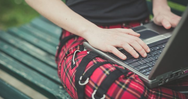 Close up of a person wearing tartan jeans with straps working on a laptop to test readers to look more closely about their unconscious biases by asking them what their first thoughts were when viewing this image