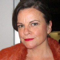 Woman with dark brown hair, red lipstick and red jacket looking directly at the viewer